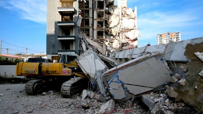 HATAY’DA AĞIR HASARLI BİNA YIKIM SIRASINDA İŞ MAKİNESİNİN ÜZERİNE DEVRİLDİ